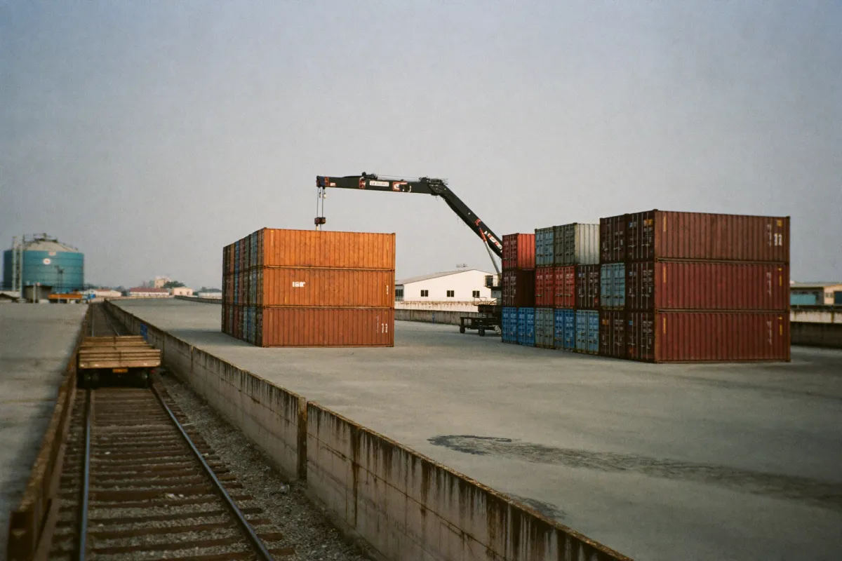 Rows of stacked shipping containers at an inland container depot, with a reach stacker and a rail siding alongside.